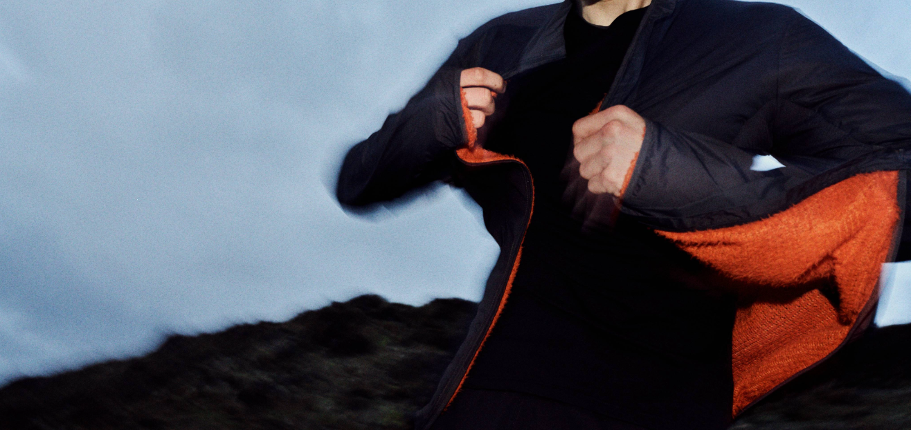 An athlete putting a jacket on over a merino long sleeve top, in twilight