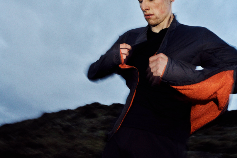 An athlete putting a jacket on over a merino long sleeve top, in twilight