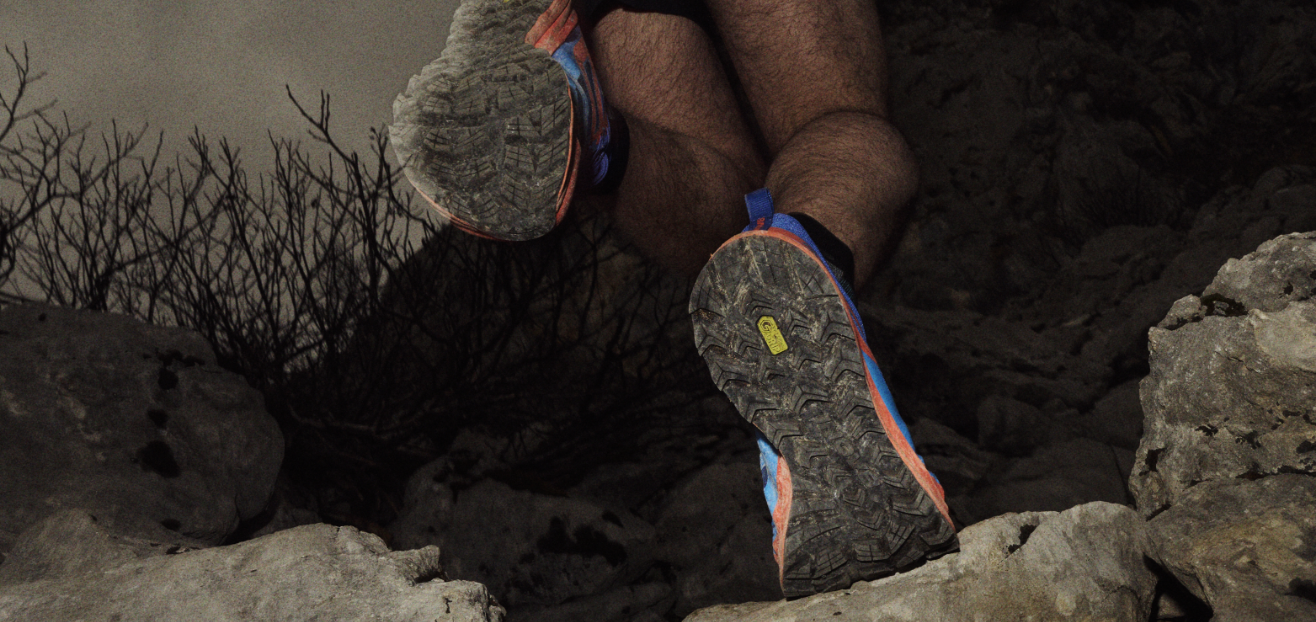View of the TRAILFLY ZERO from below, showing the sole as a runner climbs a rock