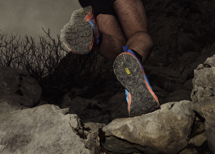 View of the TRAILFLY ZERO from below, showing the sole as a runner climbs a rock