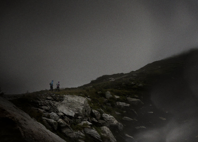 Runners in the distance on a rocky path surrounded by dark clouds