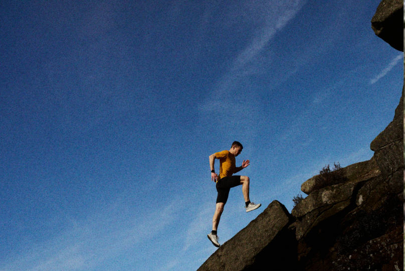 An athlete taking large steps up a steep, rocky landscape with blue skies in the background.