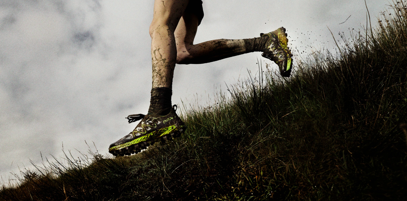 A runner's legs covered in mud, running fast down a muddy grassy field