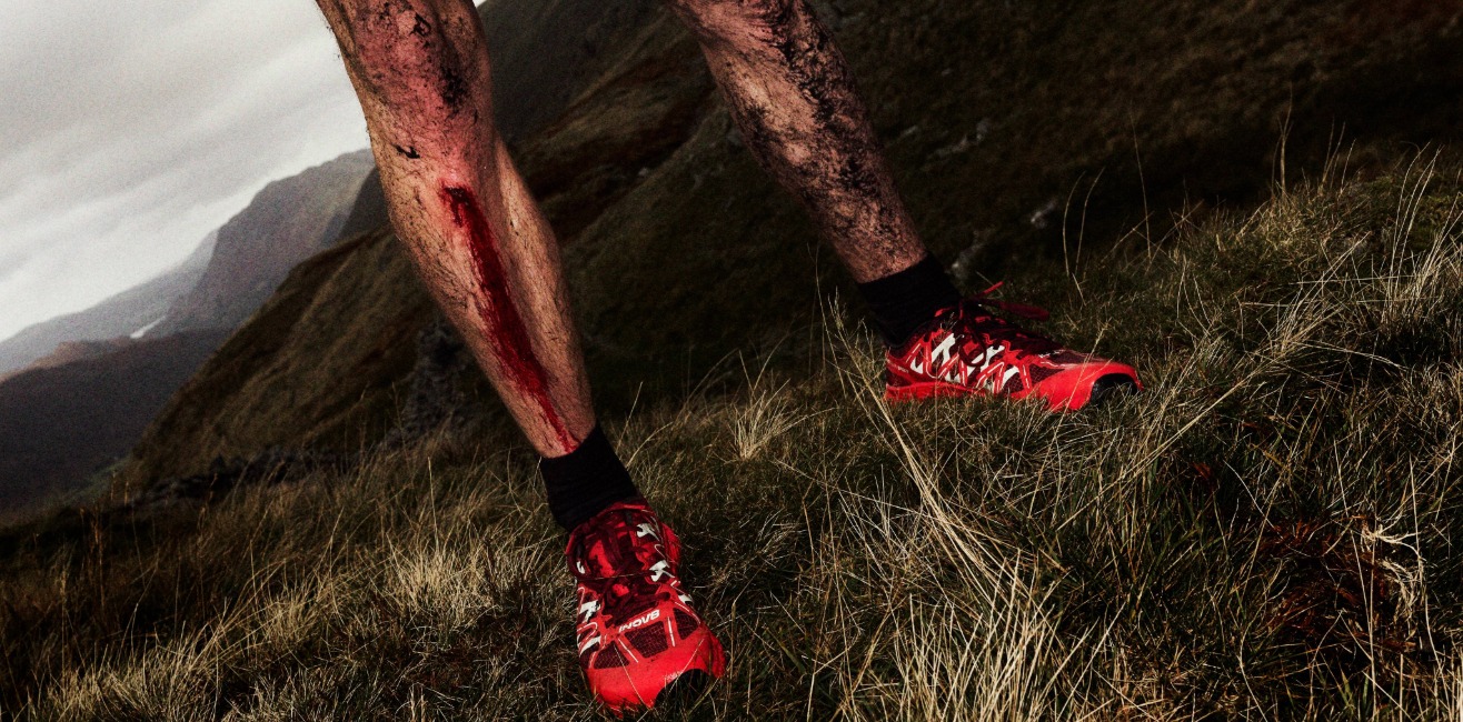 A runner's muddy and bloody leg from a slip, with the fells in the background