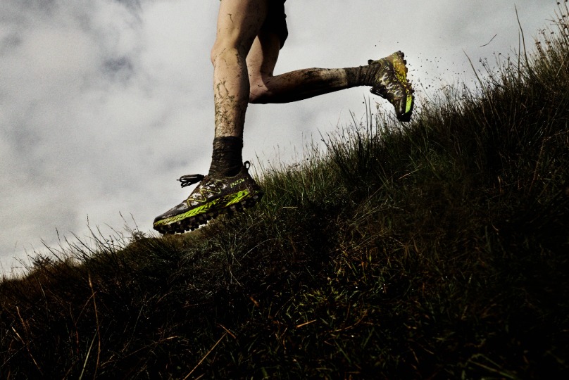 A runner's legs covered in mud, running fast down a muddy grassy field