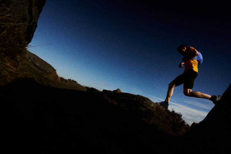 INOV8 Athlete Jack Scott running along trails with blue skies behind