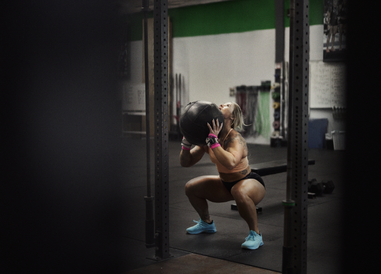 INOV8 Athlete Dani Speegle preparing to lift a large ball in a wall ball movement