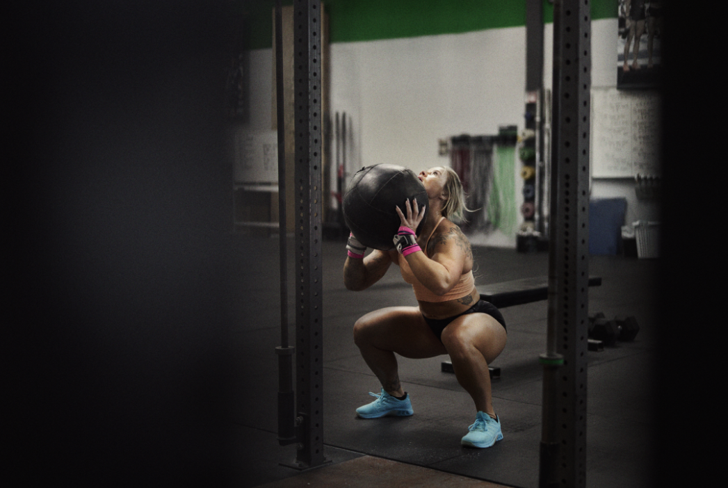 INOV8 Athlete Dani Speegle preparing to lift a large ball in a wall ball movement