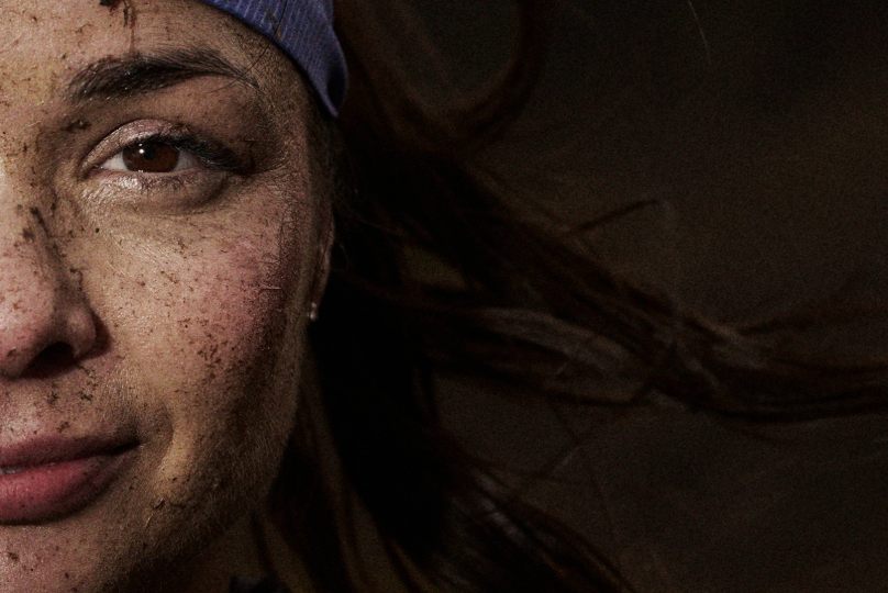 INOV8 Athlete Sarah Perry facing the camera, smiling with mud on her face
