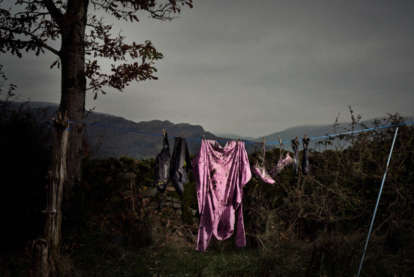 Muddy kit hung on a washing line, in front of a grey Lake District landscape.