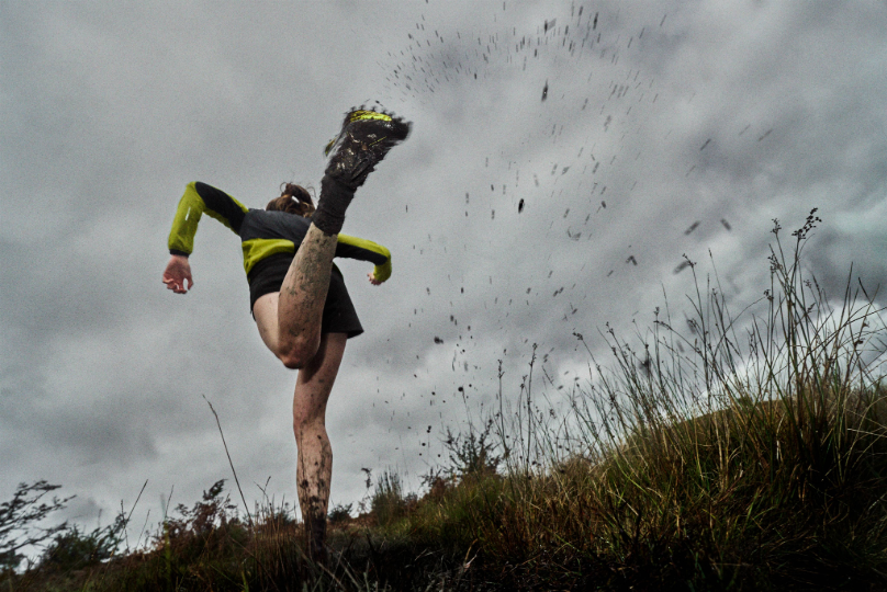A runner kicking their foot up as they run, spraying mud in the air.