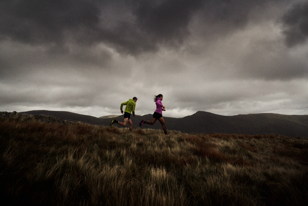 Runners in the fells, with a moody dark sky behind them.