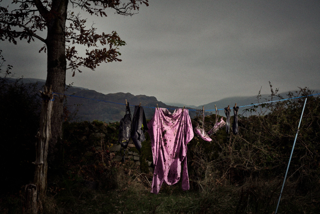 Muddy kit hung on a washing line, in front of a grey Lake District landscape.