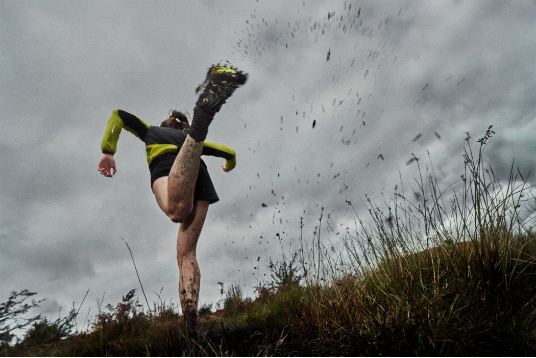 A runner kicking their foot up as they run, spraying mud in the air.