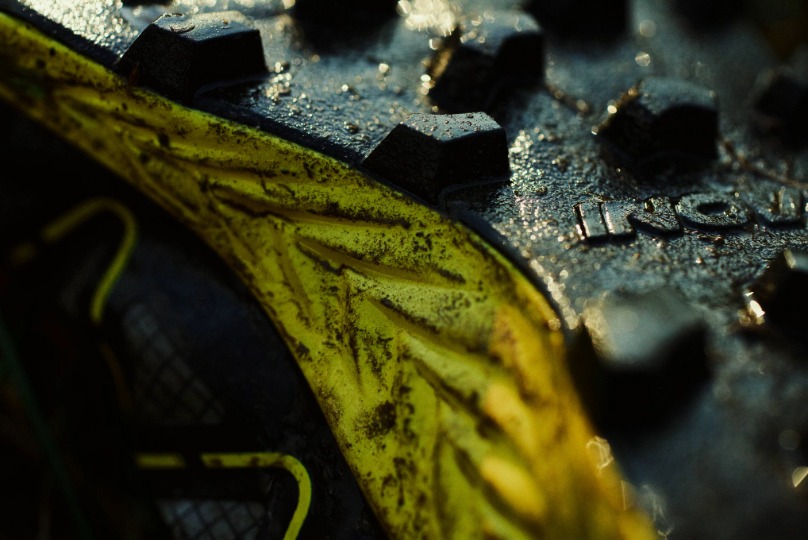 Close up shot of the aggressive lugs of a MUDTALON shoe, covered in mud