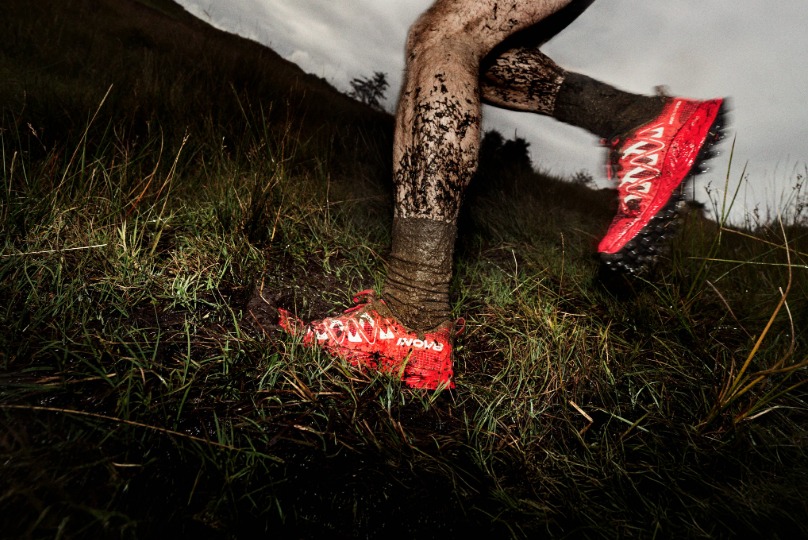 Muddy legs with bold, red shoes running through a muddy field