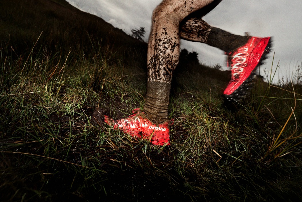 Muddy legs with bold, red shoes running through a muddy field