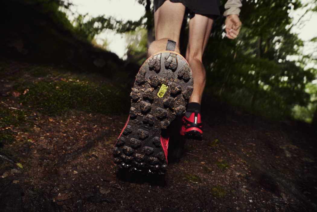 Runner running through leaves on a trail path, wearing the TRAILTALON