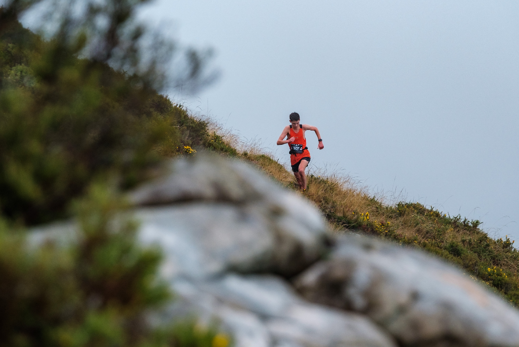 INOV8 Athlete Tom Spencer running fast down a grassy trail towards a rocky trail