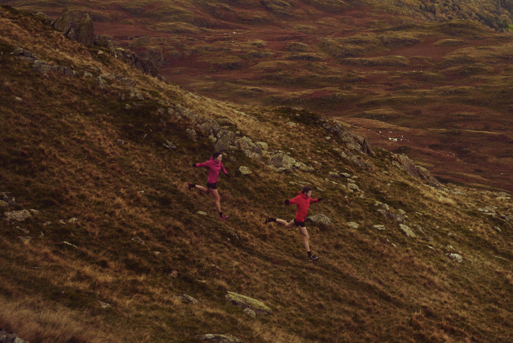 Two athletes running down a muddy fell taking long strides.