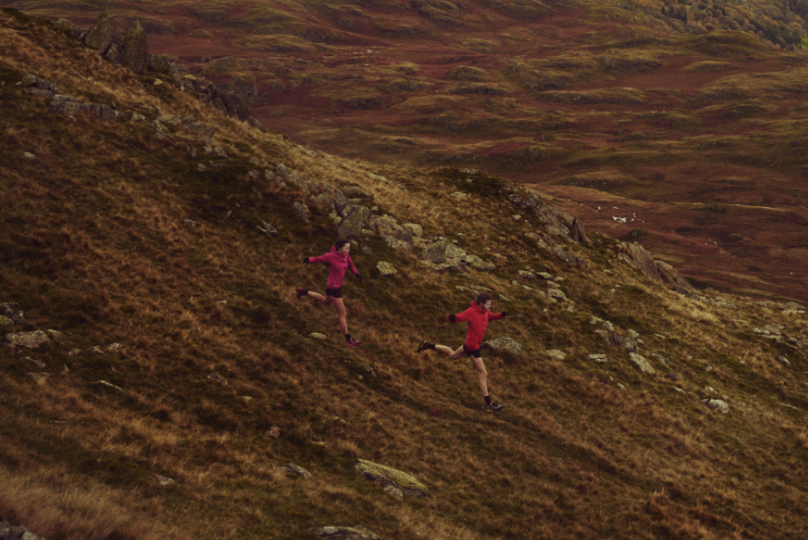 Two athletes running down a muddy fell taking long strides.