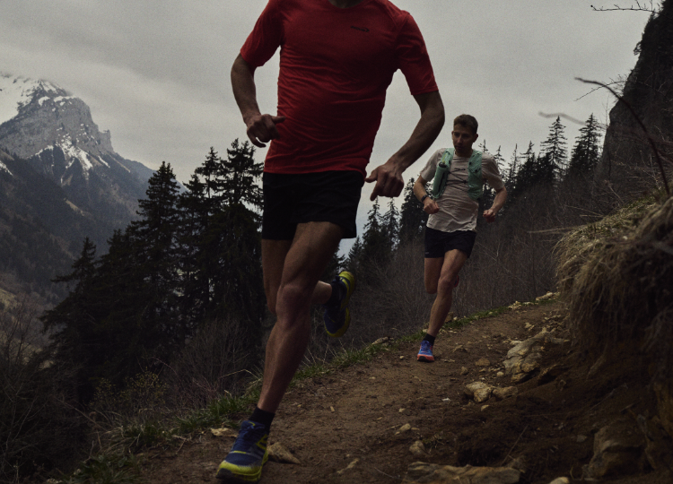Runners racing down a trail path with alpine mountains in the background.