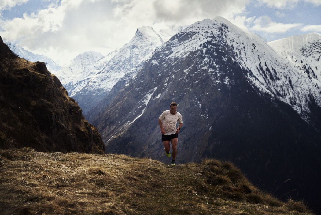INOV8 Athlete Yannick Noel summitting a large climb, with snow covered mountains in the background.