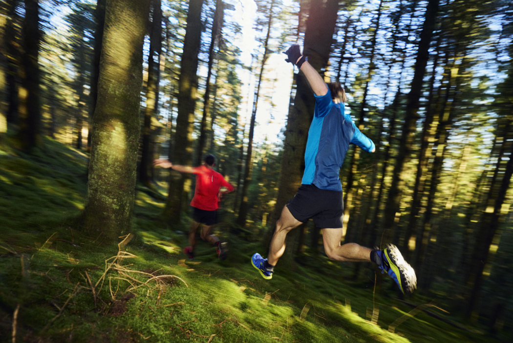 Athletes running fast down a grassy wood area, with dappled light.
