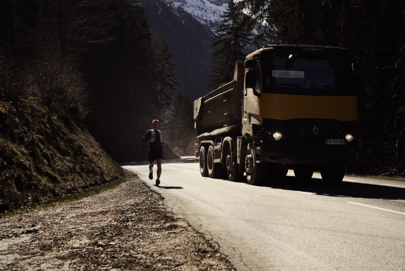 INOV8 Athlete Yannick Noel running down an alpine road, next to a large truck. 